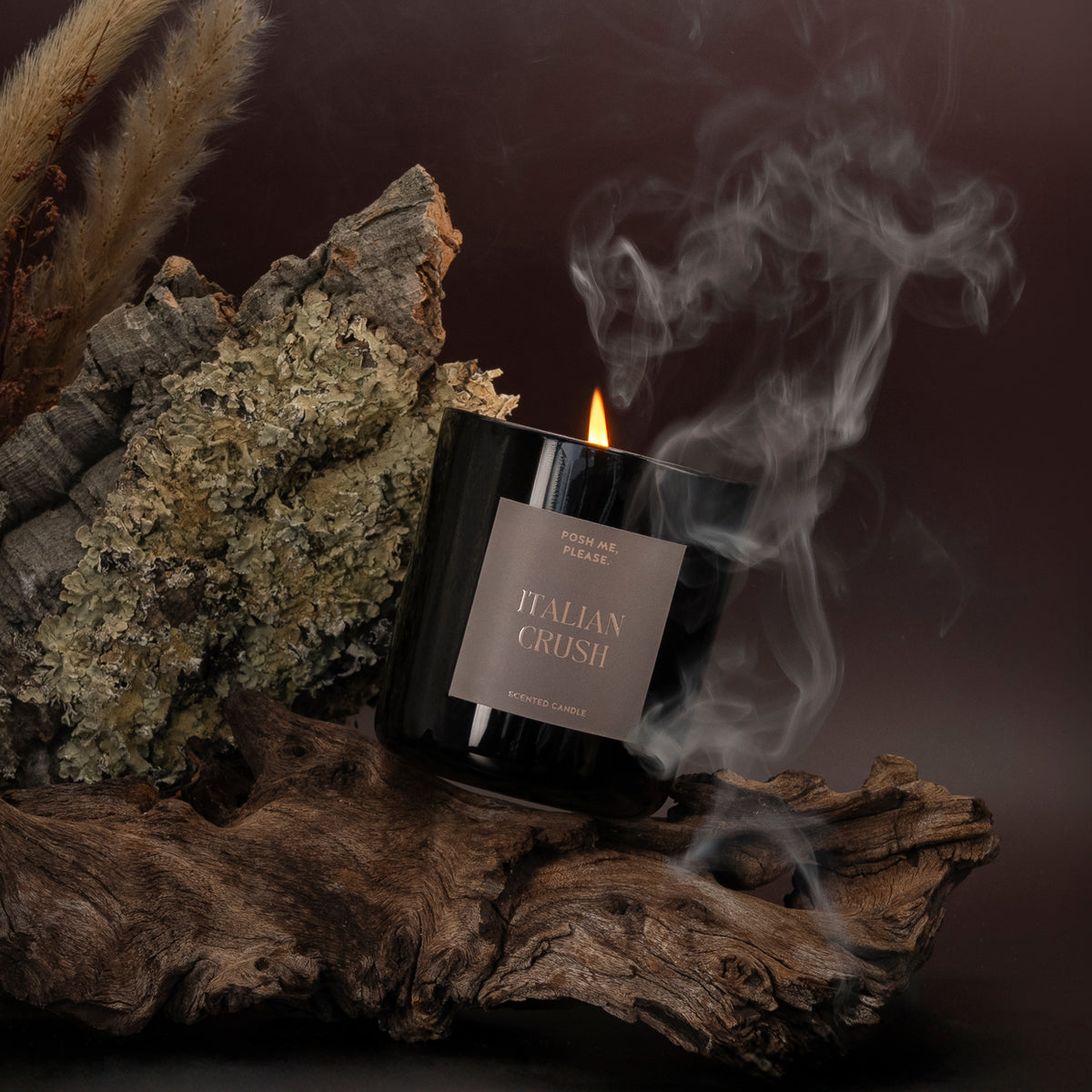 Lit Italian Crush candle with smoke wisps resting on dark bark and moss, dramatic dark background