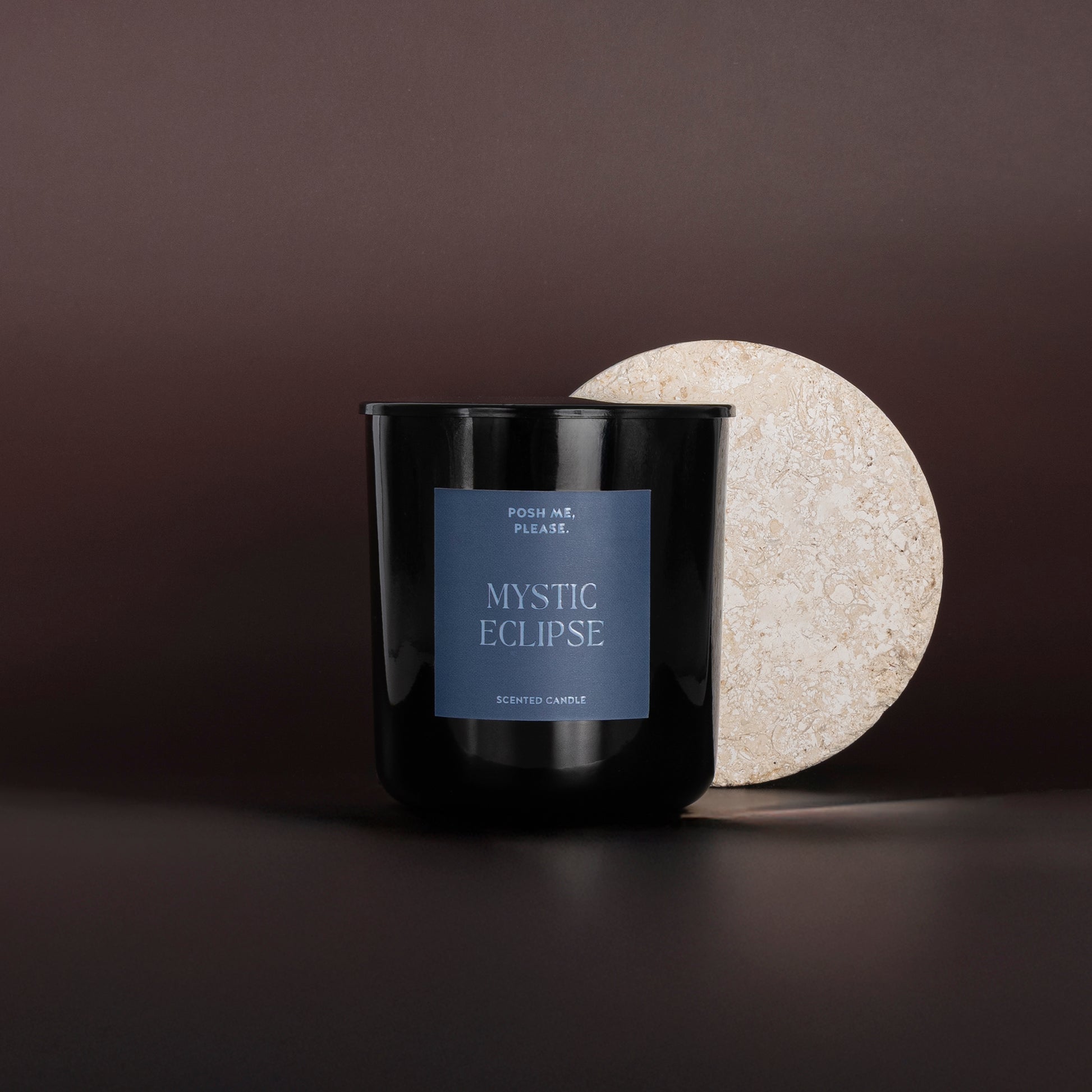 Mystic Eclipse candle beside a round textured stone disc on a dark brown surface