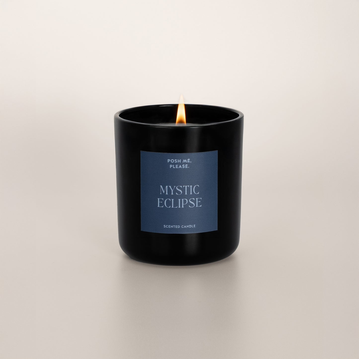 Lit Mystic Eclipse candle with flame, warm amber oriental scent, neutral background
