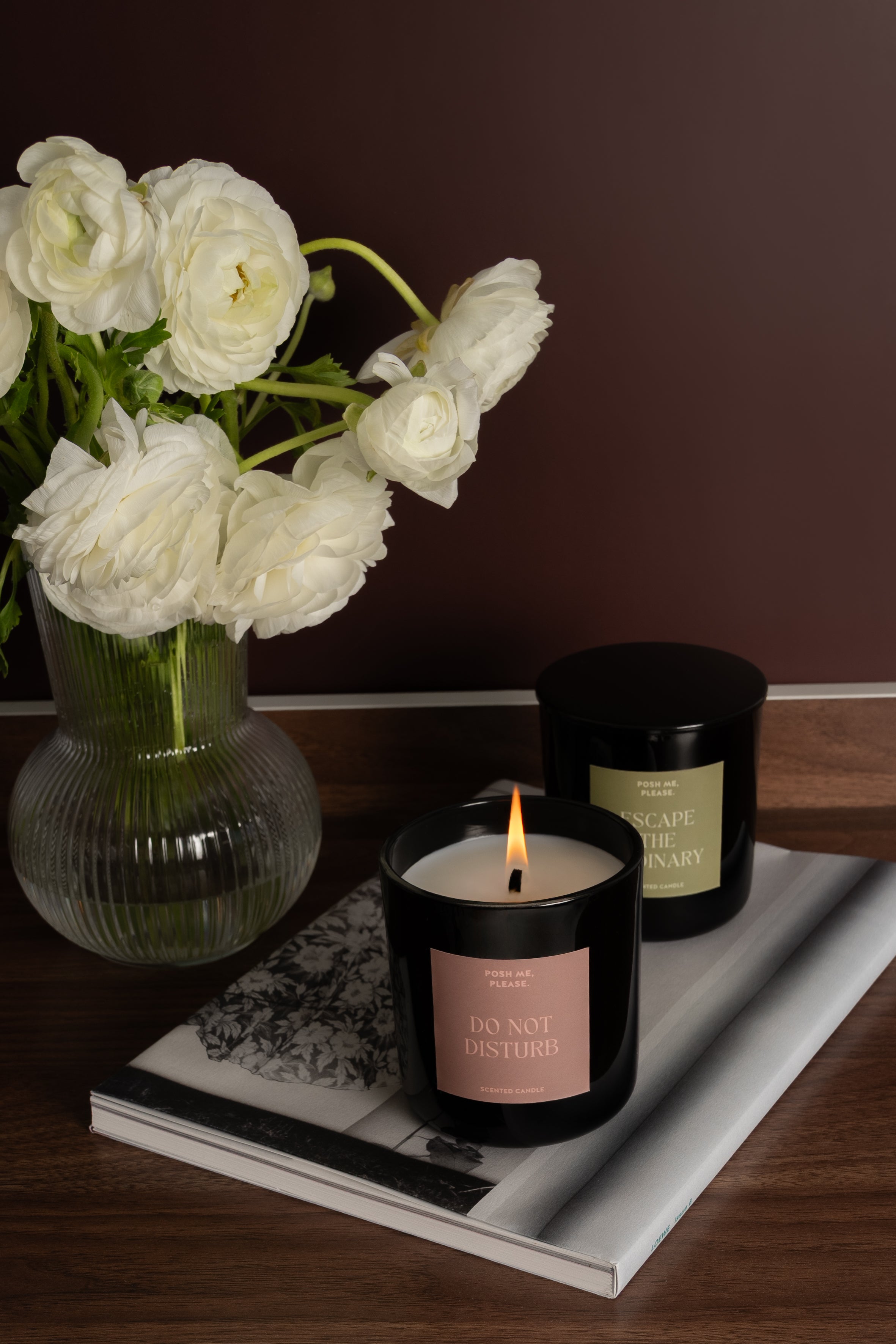 Lit Do Not Disturb and Escape the Ordinary candles on a tray beside white ranunculus in glass vase
