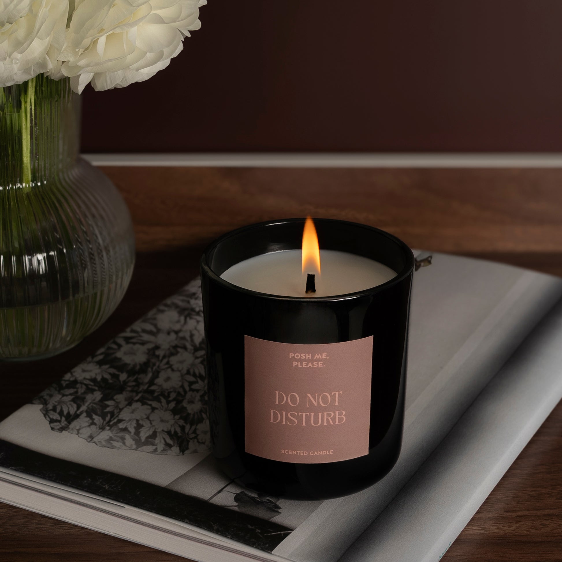 Lit Do Not Disturb candle on a dark tray with a journal, white flowers in glass vase, warm wooden background