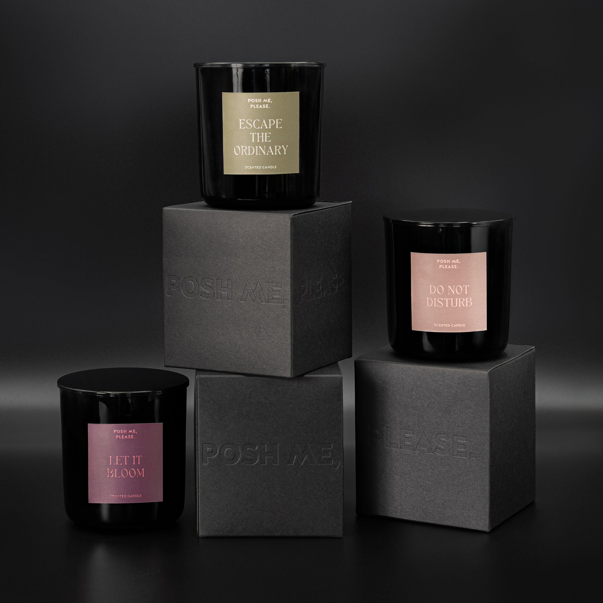 Escape the Ordinary, Do Not Disturb and Let It Bloom candles stacked on embossed POSH ME, PLEASE. black blocks, dark background