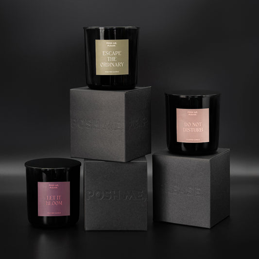 Escape the Ordinary, Do Not Disturb and Let It Bloom candles stacked on embossed POSH ME, PLEASE. black blocks, dark background