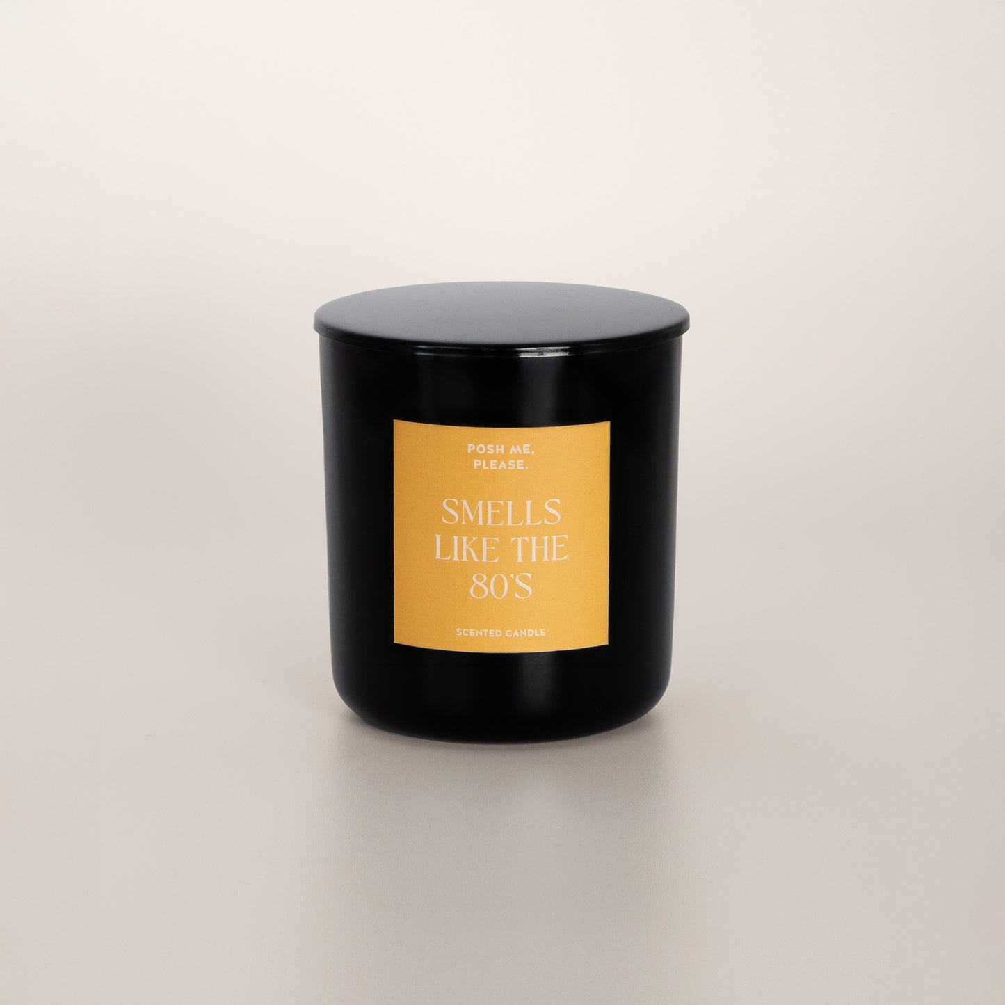 Smells Like The 80s black glass candle with golden yellow label by POSH ME, PLEASE., lid on, light background
