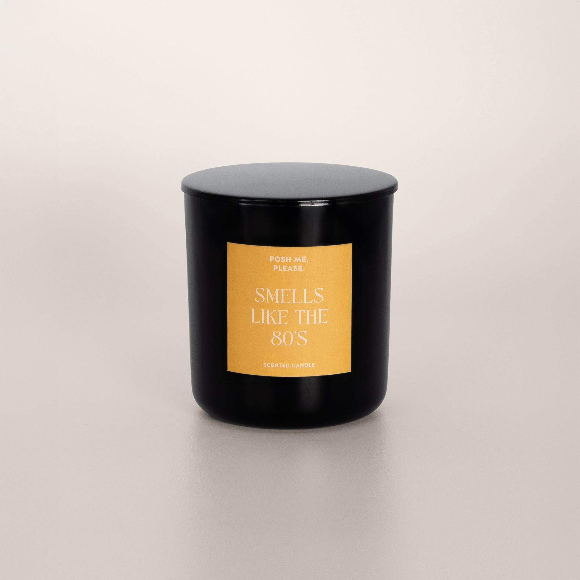 Smells Like The 80s black glass candle with golden yellow label by POSH ME, PLEASE., lid on, light background