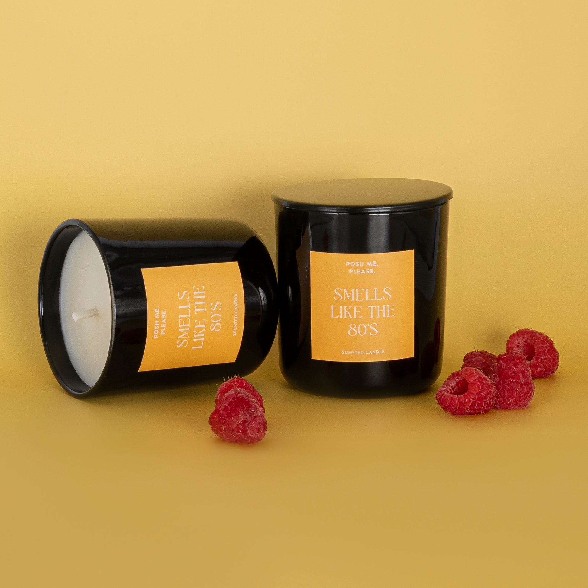 Two Smells Like The 80s candles with fresh raspberries scattered on a golden yellow background
