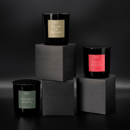 Botanica di Luna, Escape the Ordinary and Tomato Obviously candles stacked on embossed POSH ME, PLEASE. black blocks, dark background