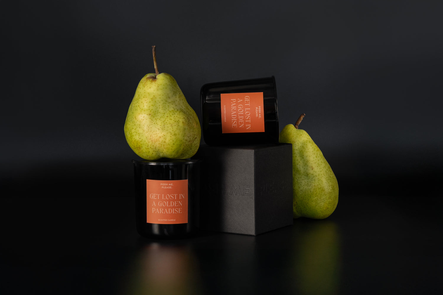Get Lost in a Golden Paradise candles stacked on black block beside green pears, dark background