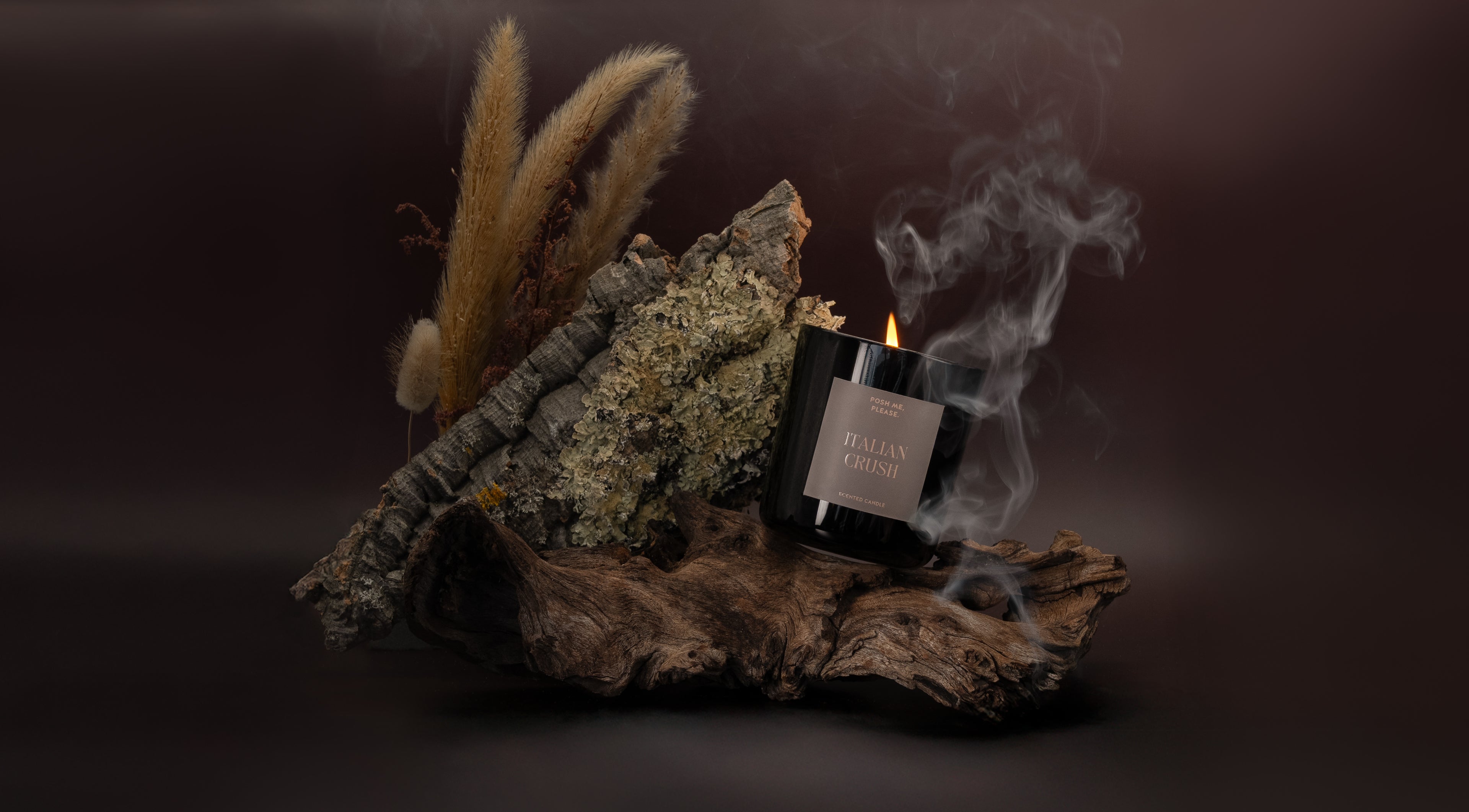 Lit Italian Crush candle with smoke wisps on dark bark and moss, dramatic dark background, POSH ME, PLEASE.